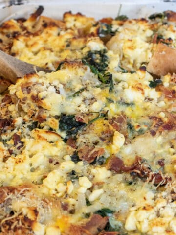 a baking dish with cheese and spinach and bacon strata.