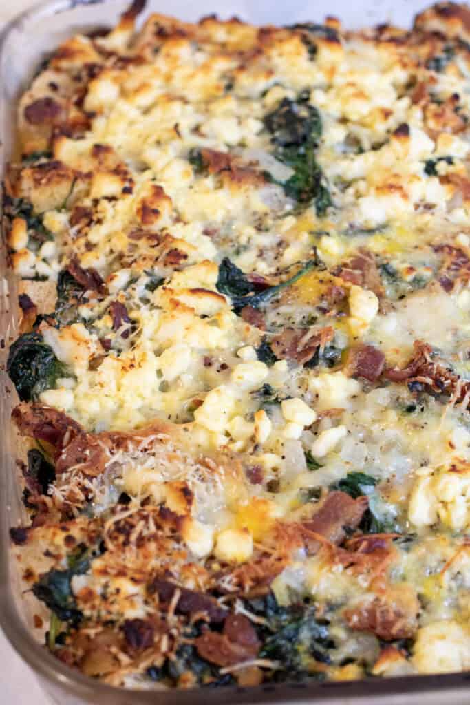 a baking dish with cheese and spinach and bacon strata.