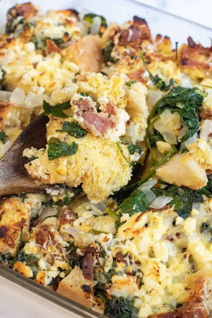 a close up of a spoon with a breakfast strata with spinach and bacon.