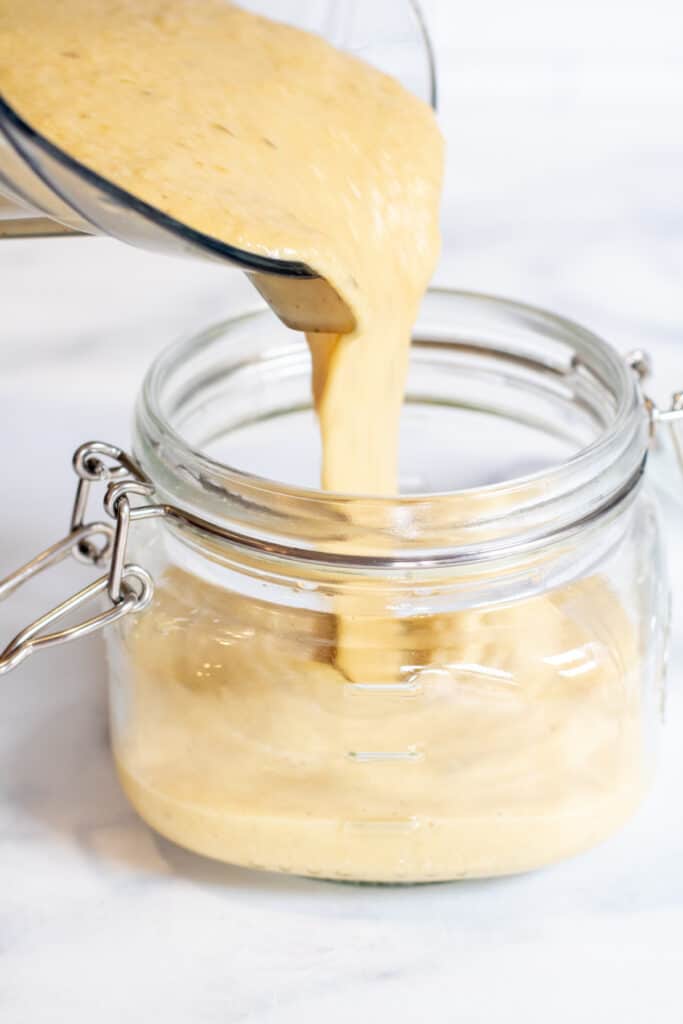 a sauce being poured into an open mason jar.