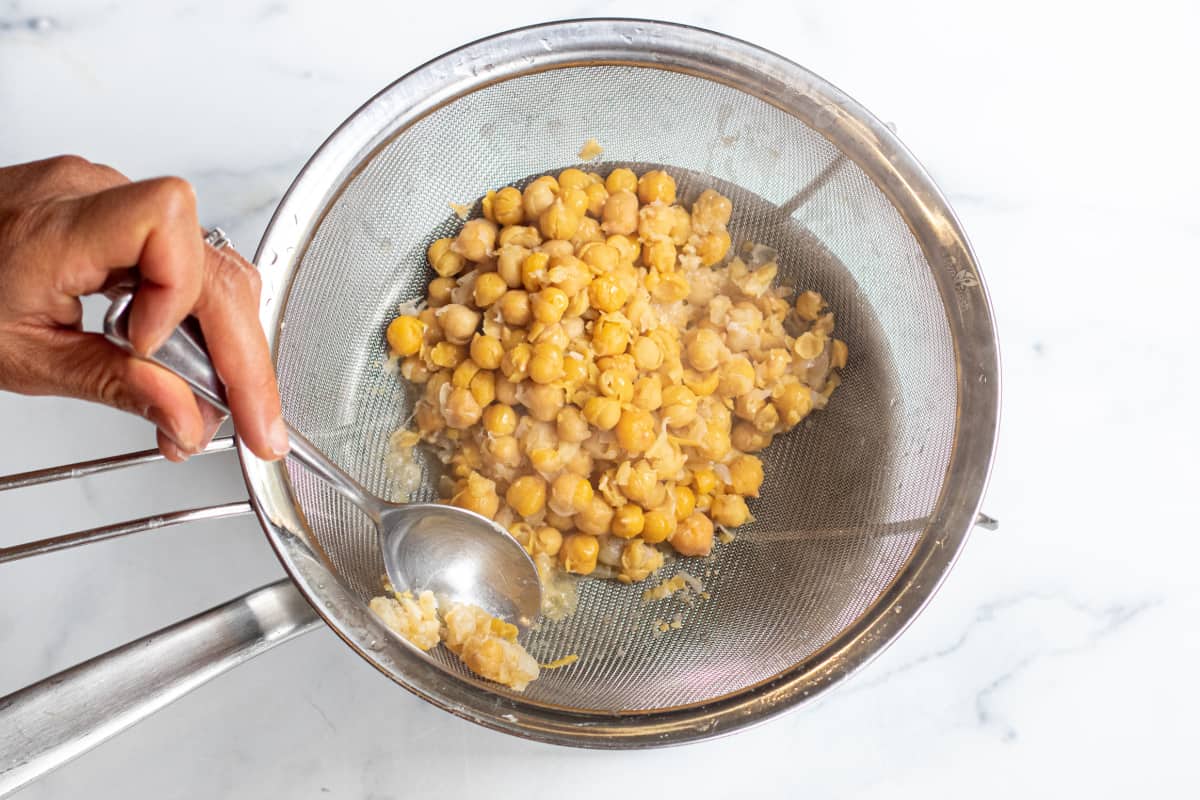 a sieve with cooked chickpeas and hand and spoon.