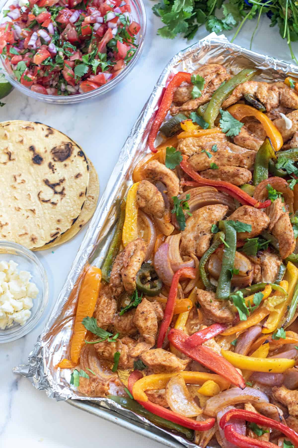 a sheet pan of chicken fajitas, corn tortillas, pico, and cheese.