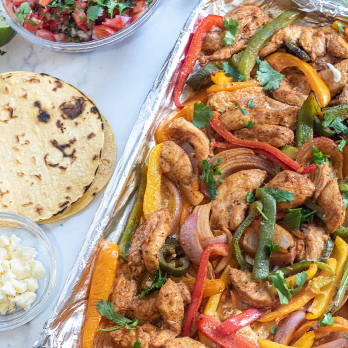 a sheet pan of chicken fajitas, corn tortillas, pico, and cheese.