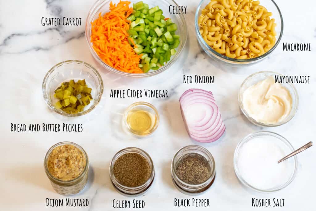 macaroni, celery, carrot, pickle, mayo, spices, dijon, salt on a counter.