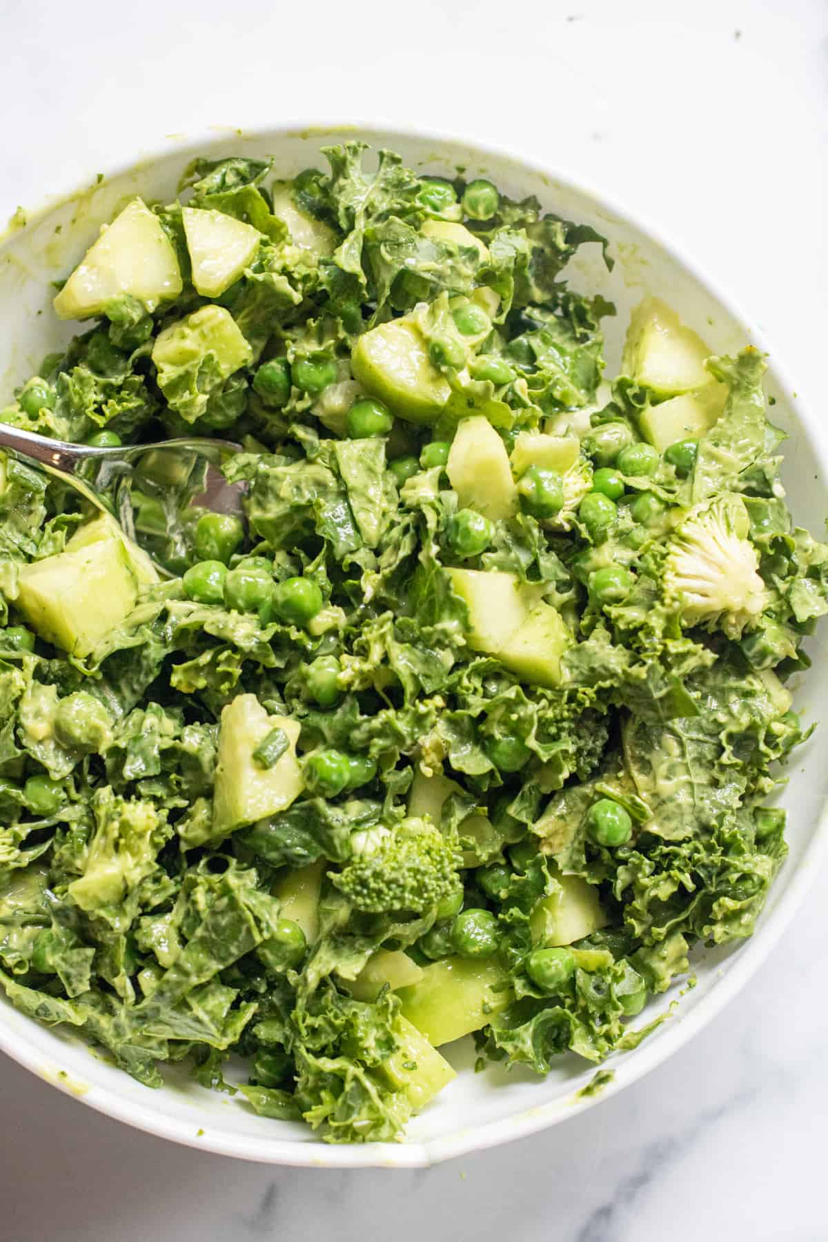 a bowl of salad of kale, cucumbers, peas, and a green dressing.