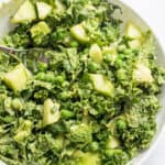 a bowl of salad of kale, cucumbers, peas, and a green dressing.
