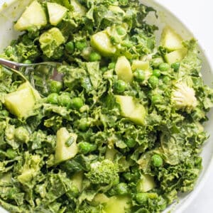 a bowl of salad of kale, cucumbers, peas, and a green dressing.