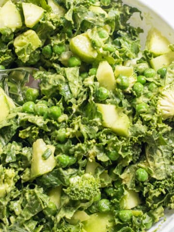 a bowl of salad of kale, cucumbers, peas, and a green dressing.