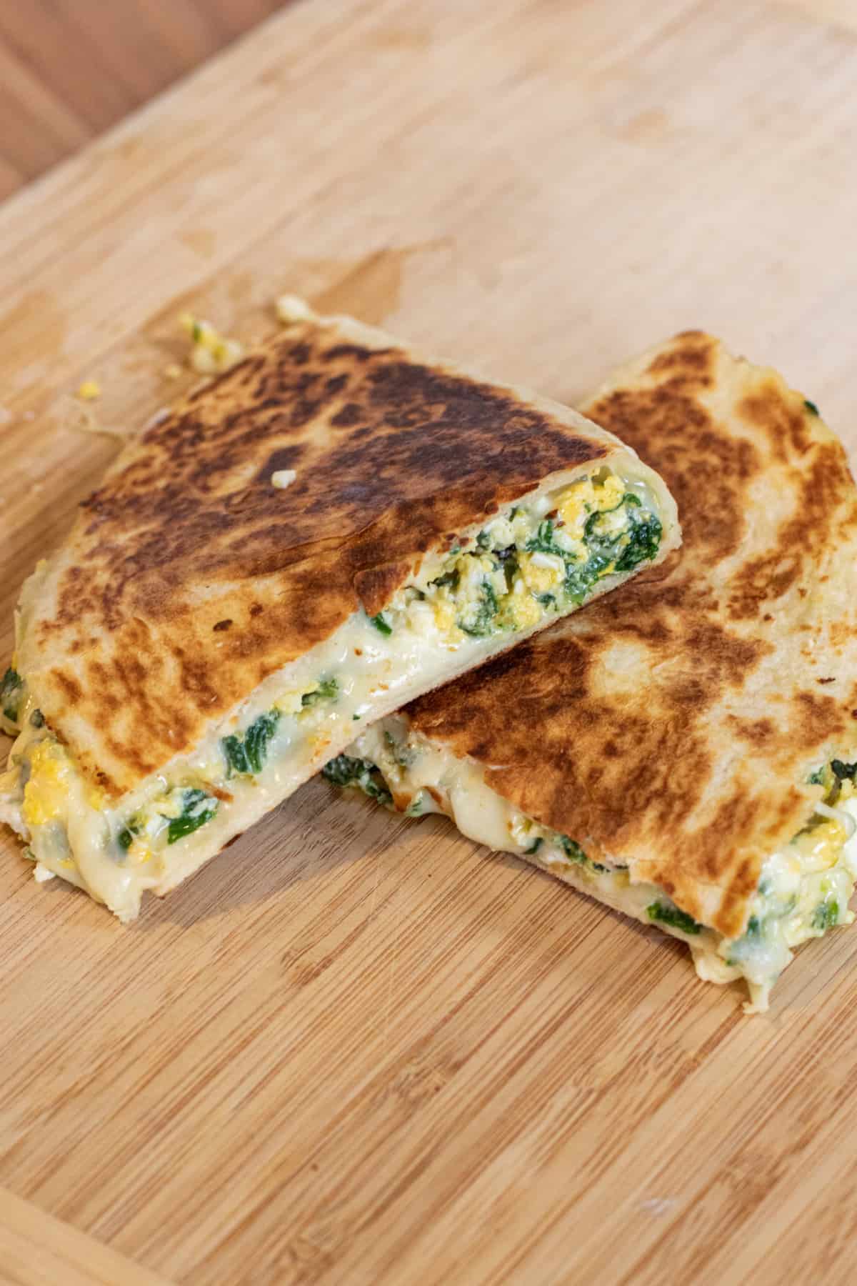 a quesadilla with spinach and cheese on a cutting board.