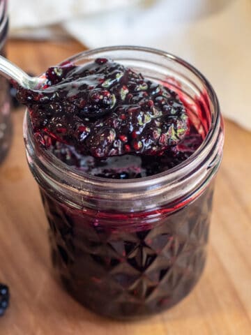 a jar of open blackberry jam with a spoon of jam.