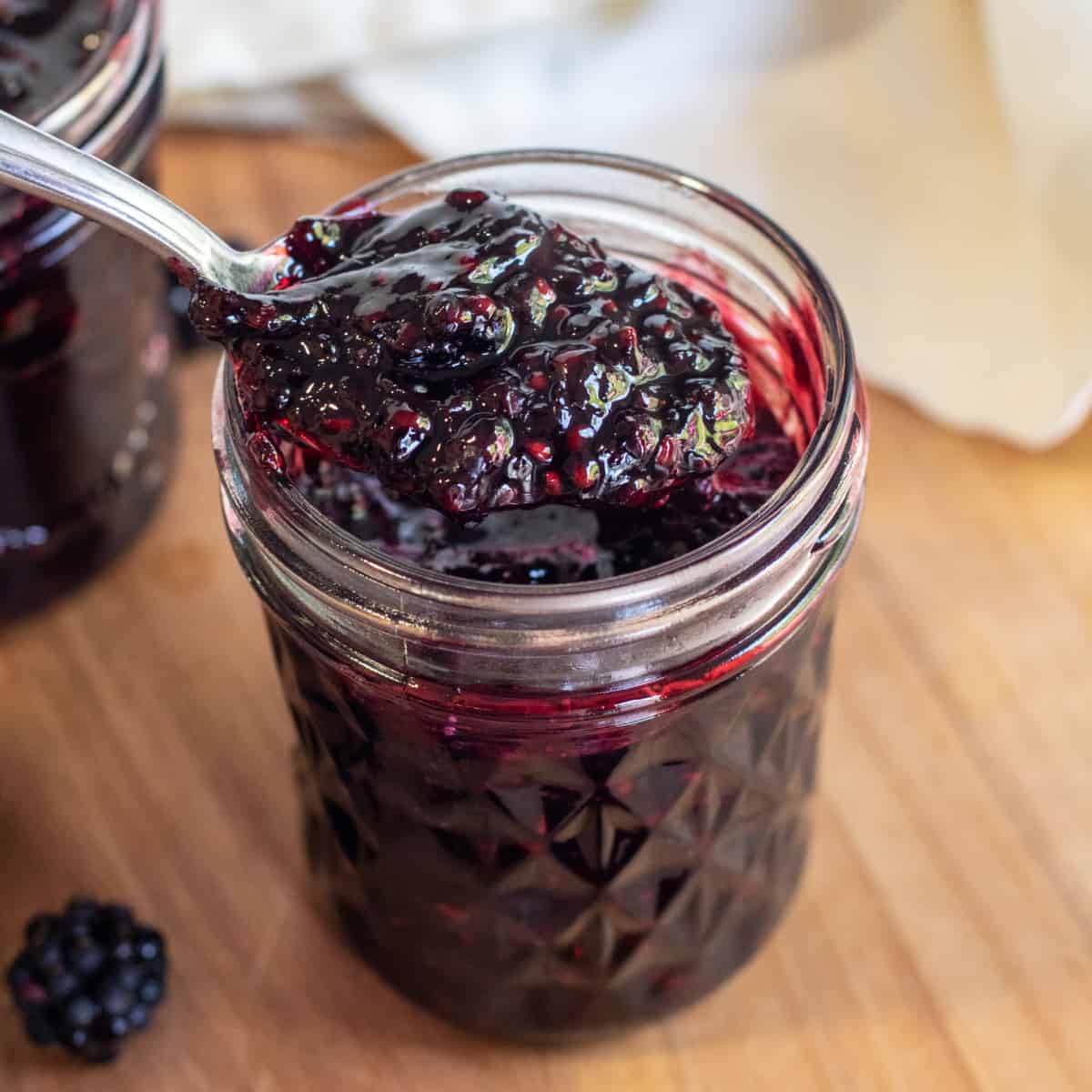 a jar of open blackberry jam with a spoon of jam.