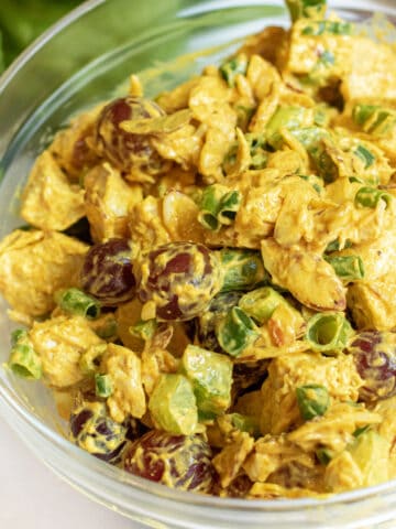 a bowl of curry chicken salad with grapes and green onions.