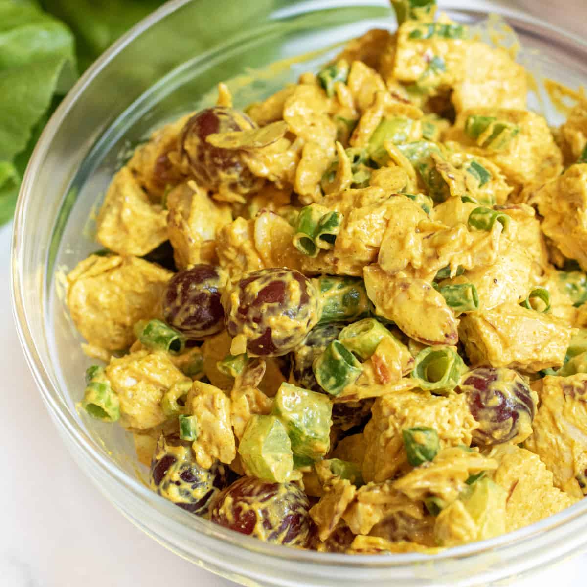 a bowl of curry chicken salad with grapes and green onions.