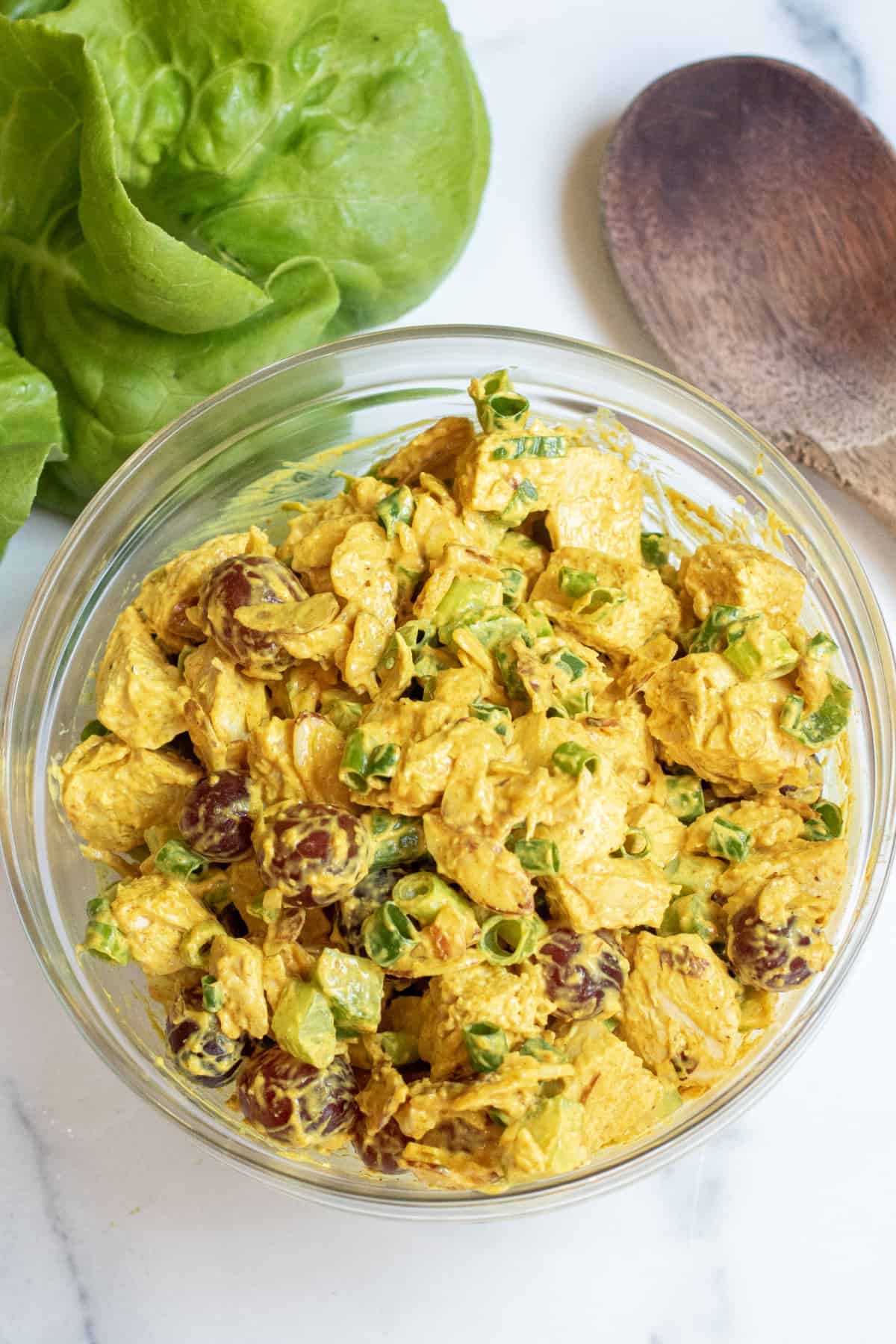 a bowl of curry chicken salad with grapes and green onions.