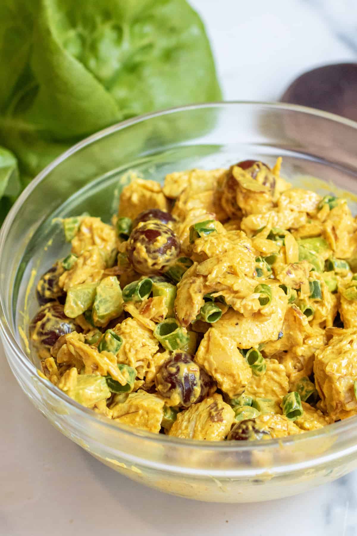 a bowl of curry chicken salad with grapes and green onions.