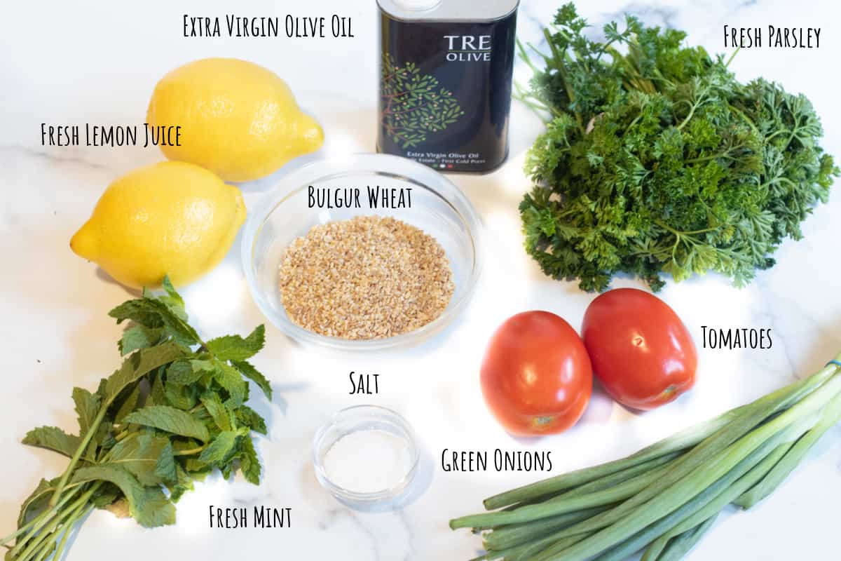 parsley, bulgur, lemons, tomatoes, onions, mint, oil, and salt on a counter.