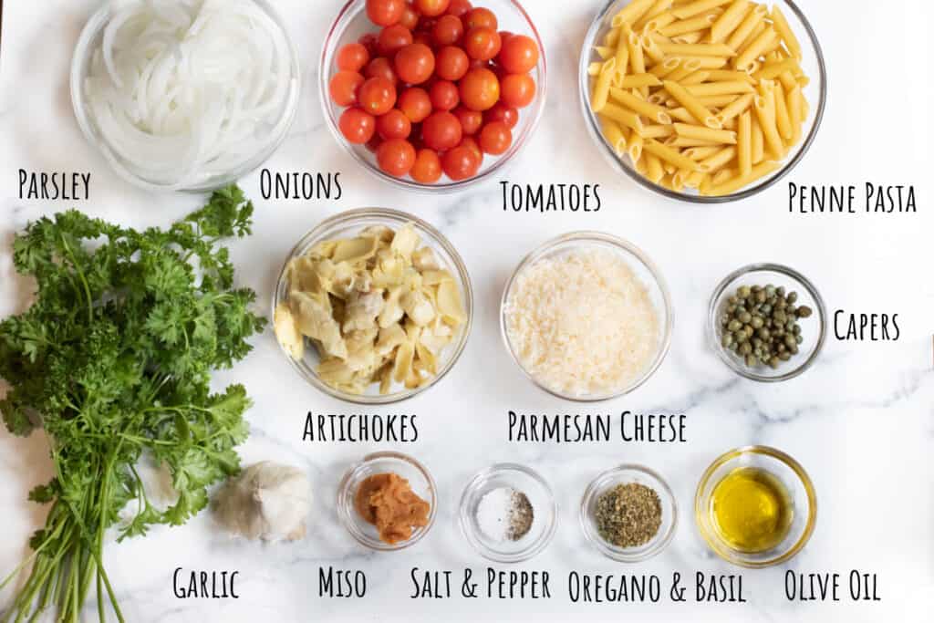 onions, tomatoes, penne, parsley, artichokes, parm cheese, capers, garlic, miso, spices, salt and pepper and olive oil in bowls.