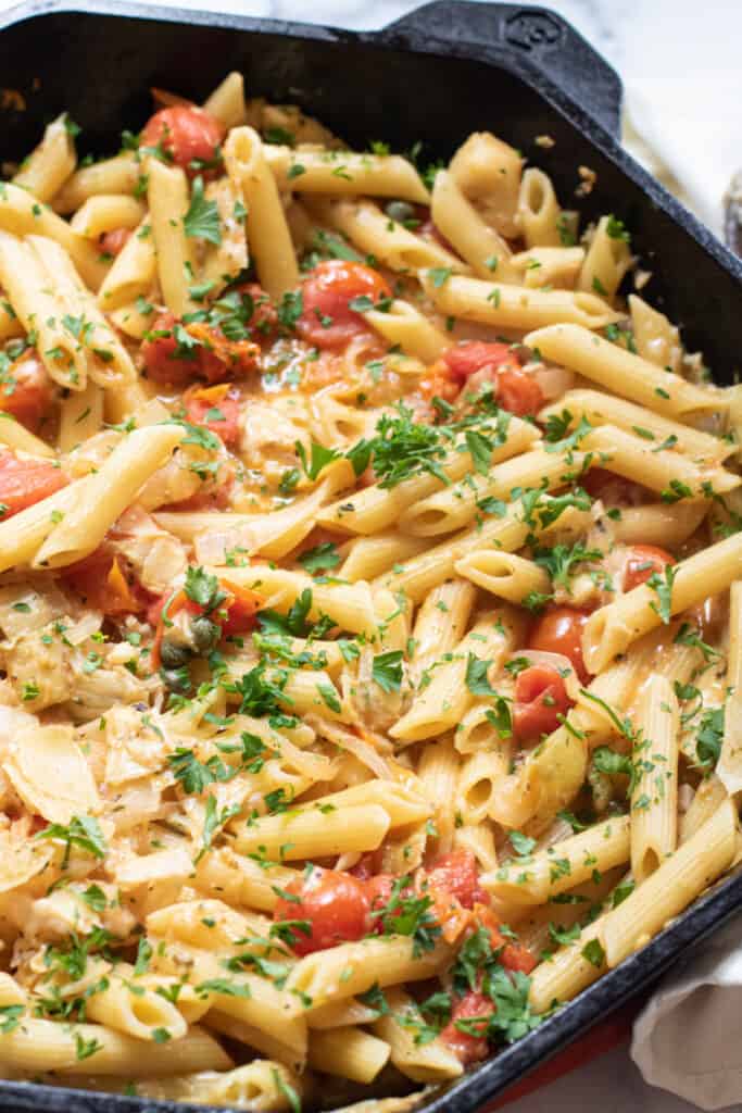 a cast iron of penne pasta with tomatoes and artichokes and parsley.