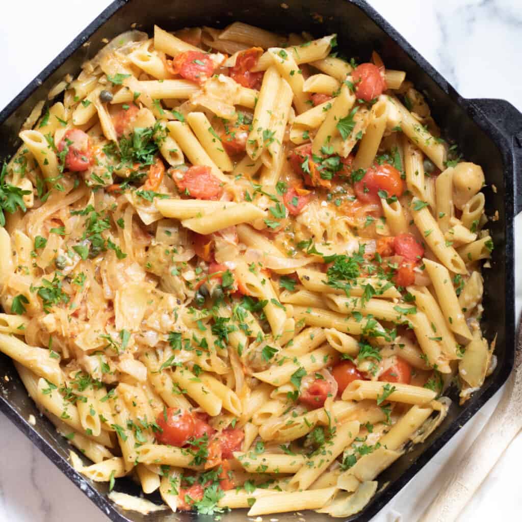 a cast iron of penne pasta with tomatoes and artichokes and parsley.