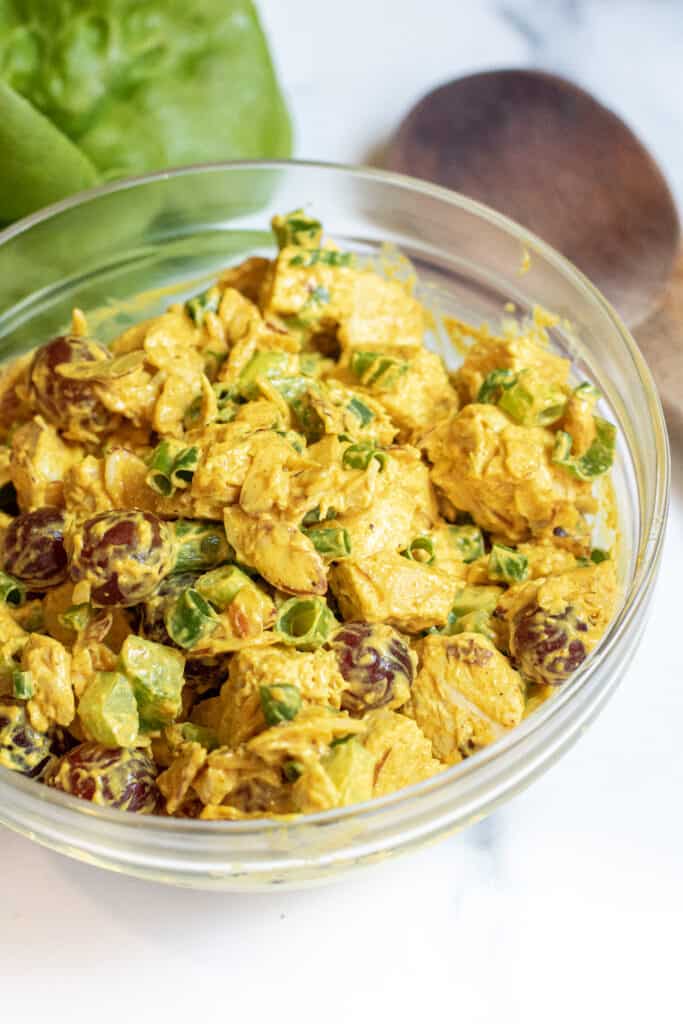 a bowl of curry chicken salad with grapes and green onions.