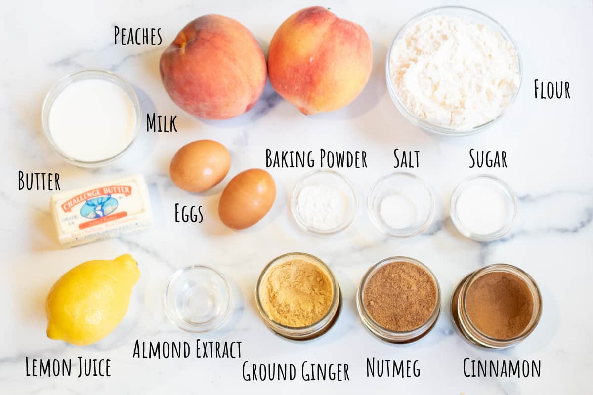 peaches, lemon, milk, butter, spices, eggs, and small bowls on a counter labeled.