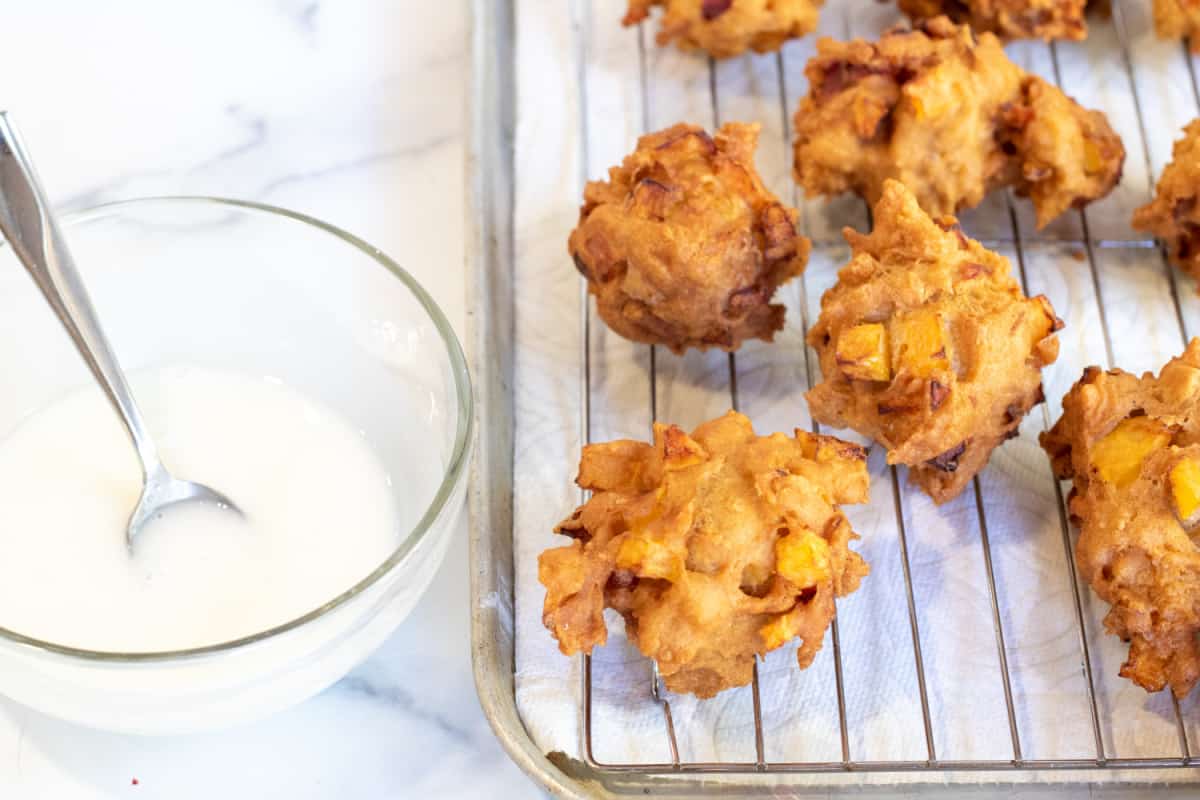 a bowl of icing next to fried fritters. 