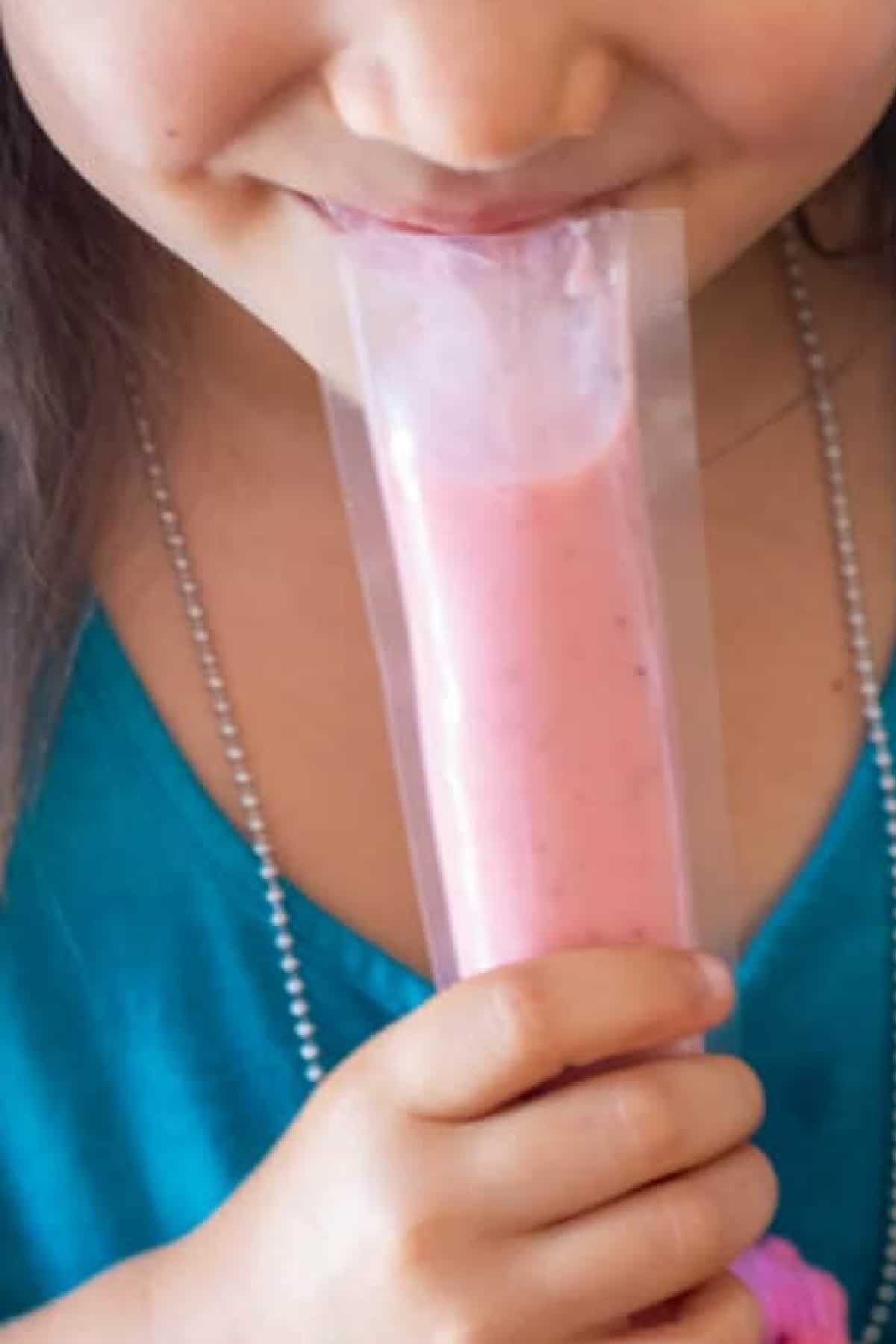 little girl holding and eating a gogurt.