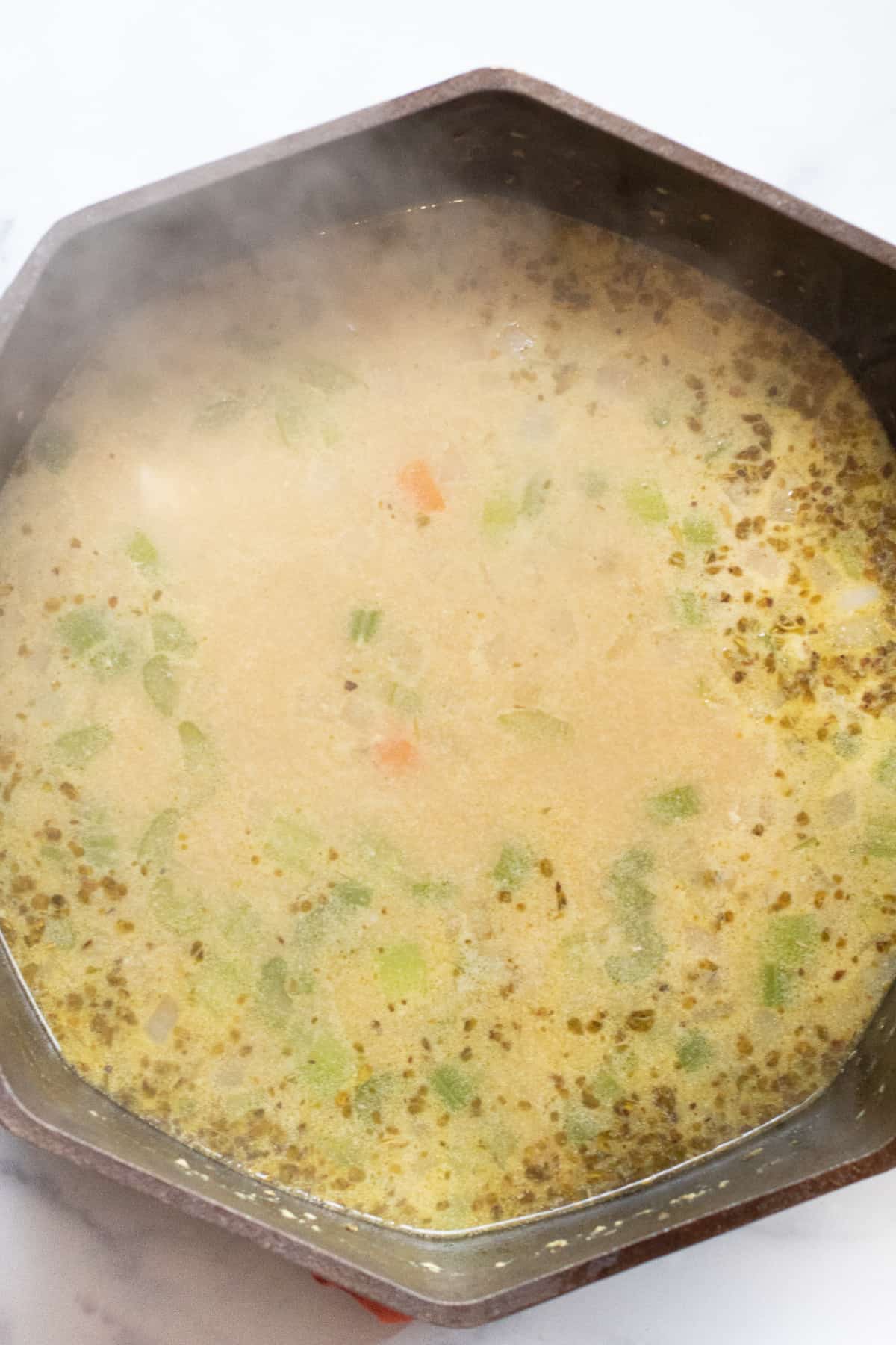 a dutch oven of soup with spices and celery and carrots. 