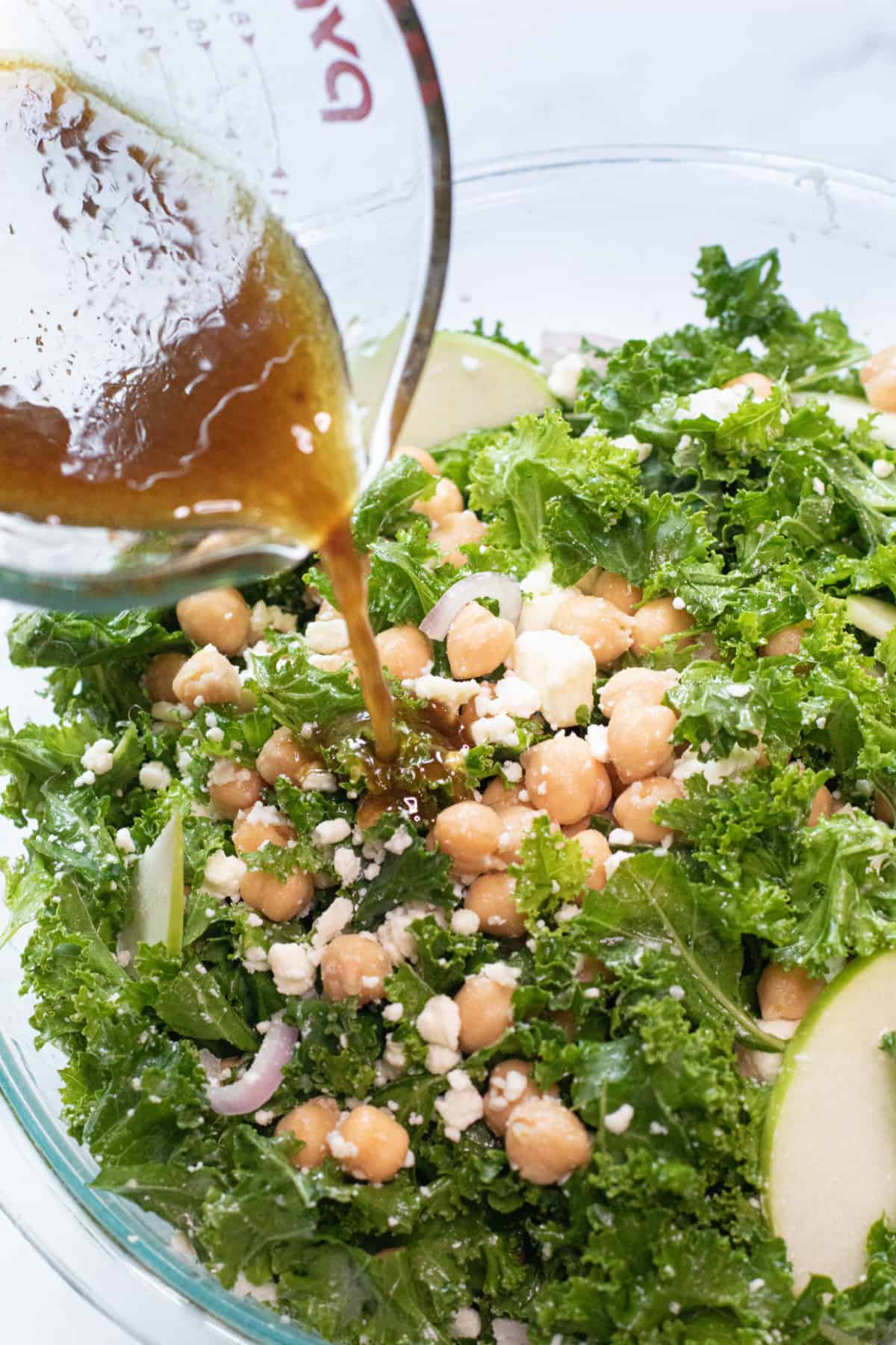 vinaigrette being poured in a bowl of kale, chickpea salad.
