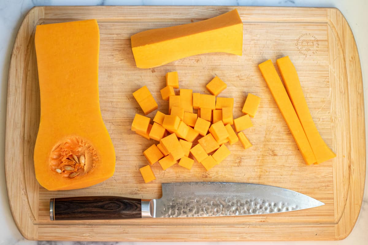 a halved and cubed butternut squash on a cutting board with a knife.