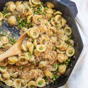 a cast iron with a wooden spoon scooping pasta with peas and pancetta.