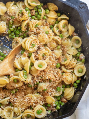 a cast iron with a wooden spoon scooping pasta with peas and pancetta.