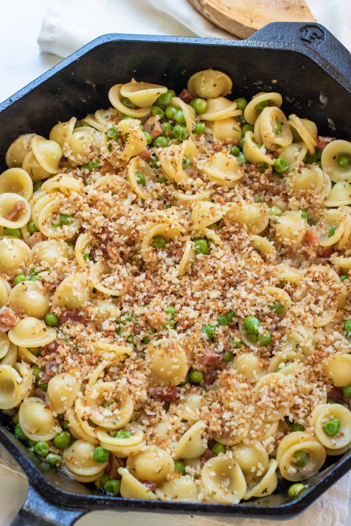 a cooked pasta dish with peas, pancetta, and topped with toasted breadcrumbs.
