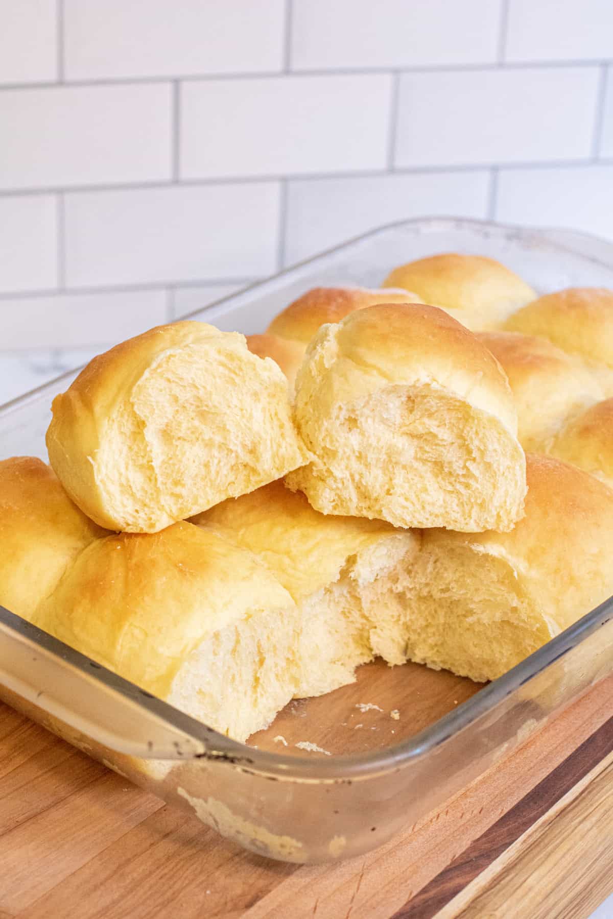 two Hawaiian rolls out of a pan of rolls sitting on the other rolls.