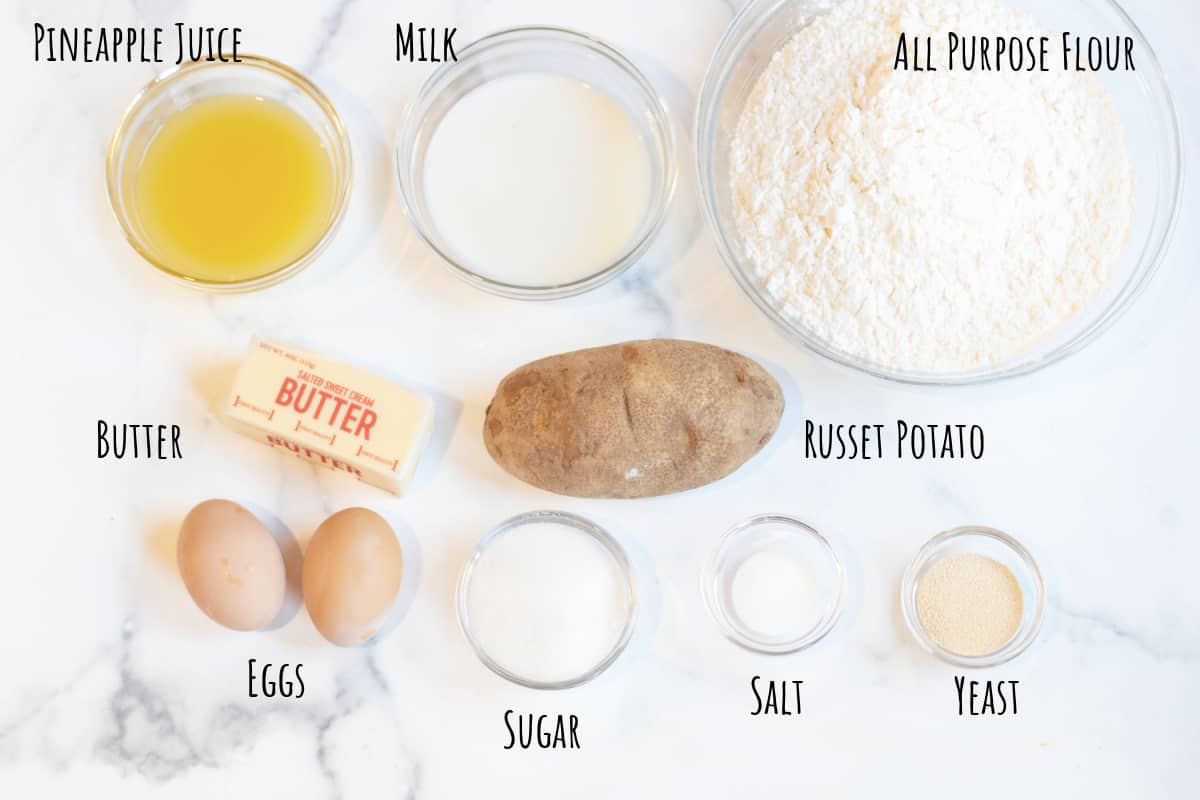 pineapple juice, sugar, flour, milk, eggs, potatoes, yeast, salt, butter on a counter.