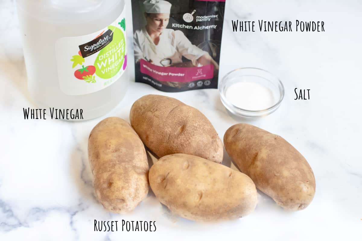 potatoes, vinegar, vinegar powder, and a bowl of salt on a counter.