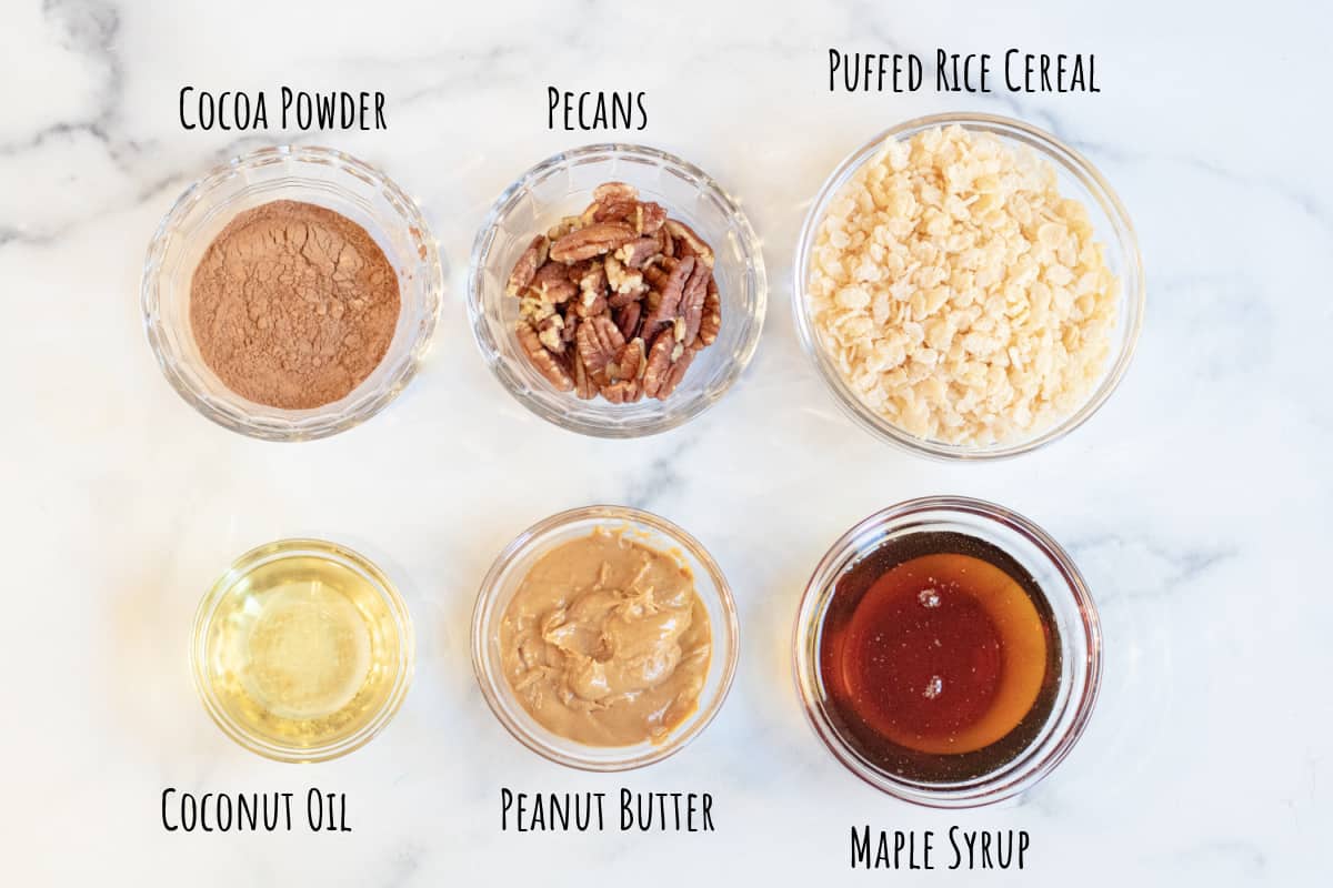 bowls of cocoa powder, pecans, rice cereal, oil, peanut butter, and maple syrup.