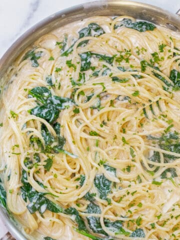 a pan with spaghetti with cream sauce and spinach.
