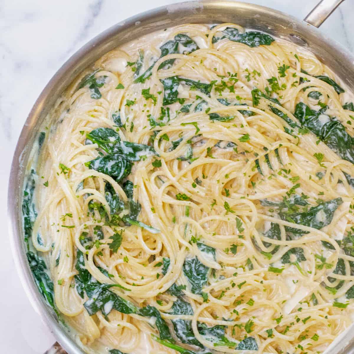 a pan with spaghetti with cream sauce and spinach.