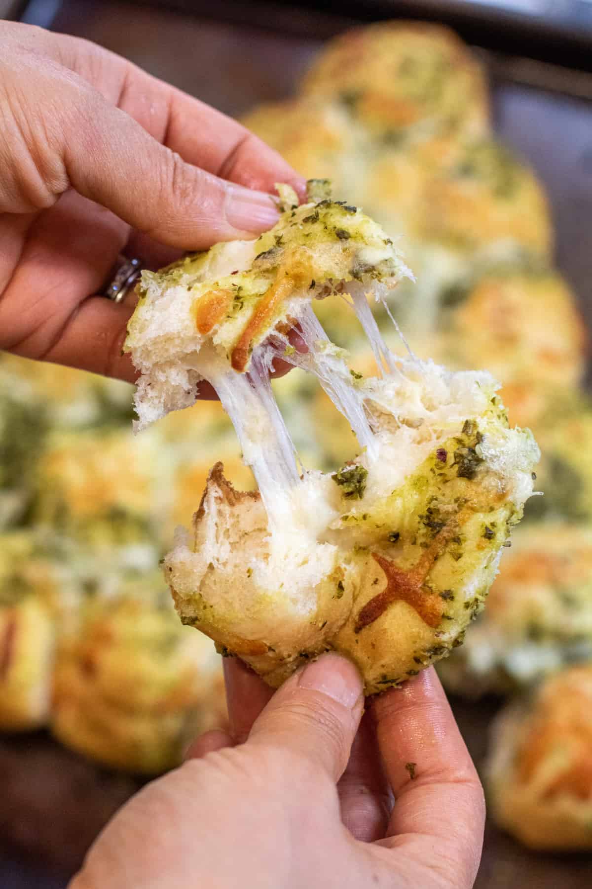 a hand pulling apart a cheesy roll.