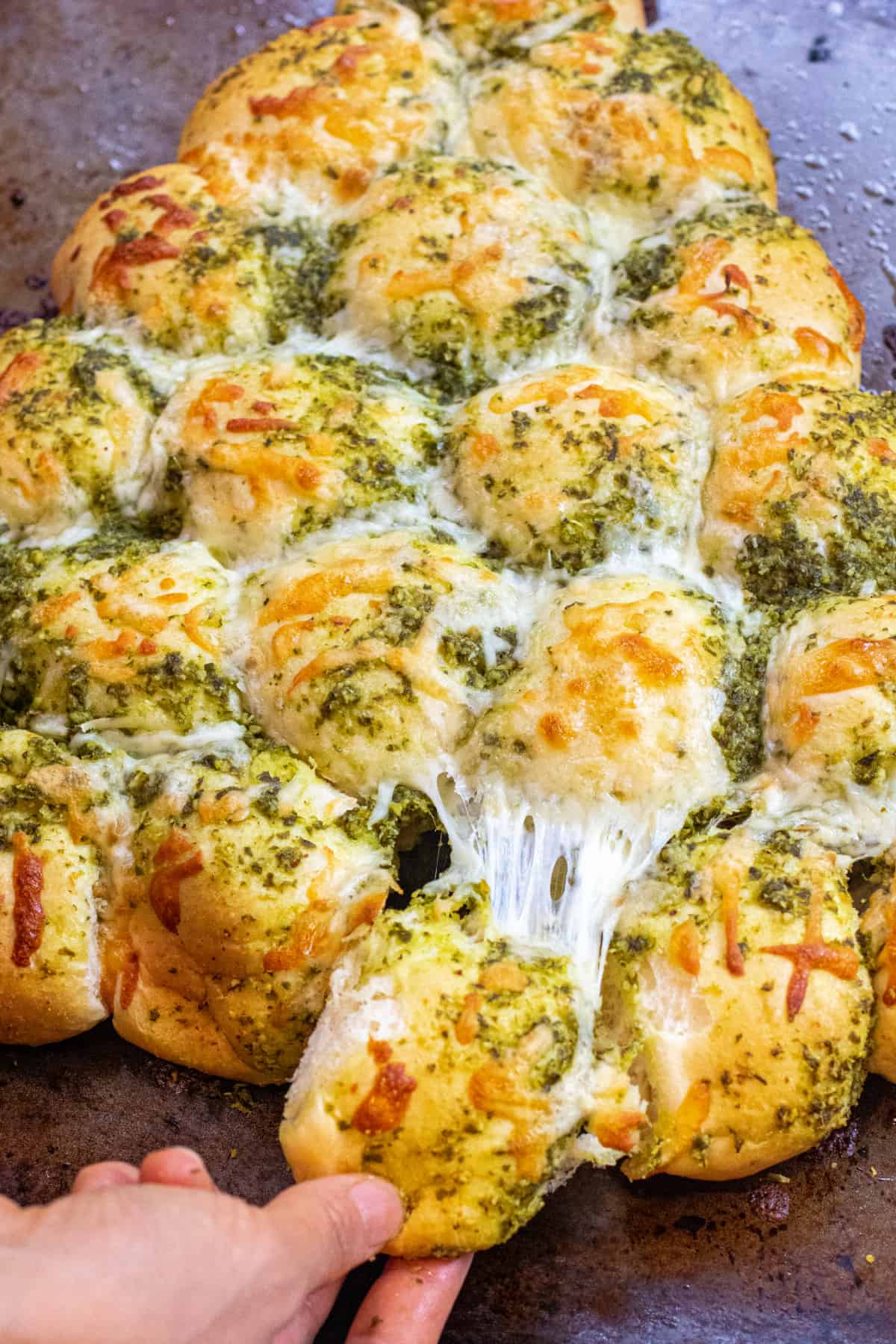 a hand pulling a cheesy pesto covered roll out from a bunch of rolls.