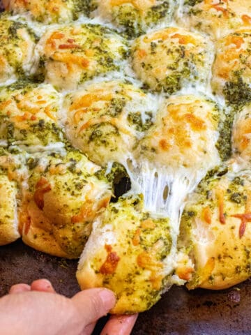 a hand pulling a cheesy pesto covered roll out from a bunch of rolls.