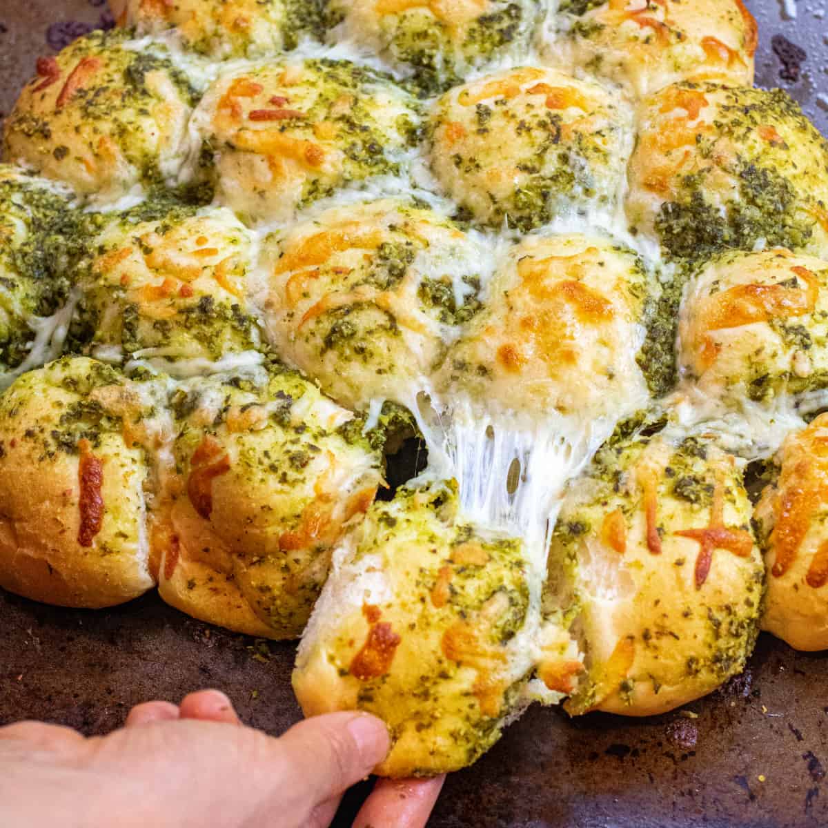 a hand pulling a cheesy pesto covered roll out from a bunch of rolls.