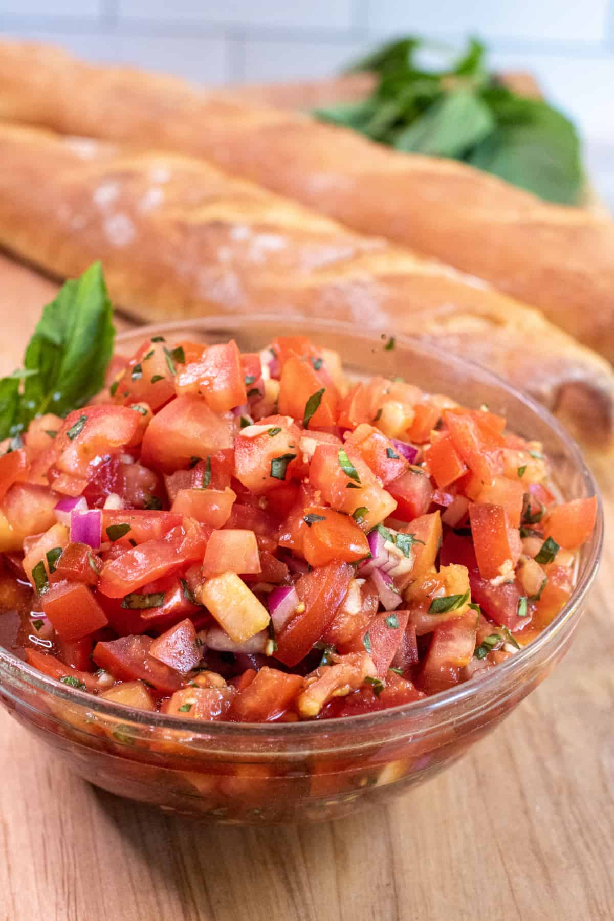 a bowl of bruschetta in front of two baguettes.