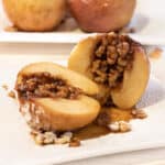 a halved baked apple with walnuts inside on a plate.