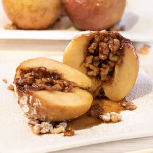 a halved baked apple with walnuts inside on a plate.