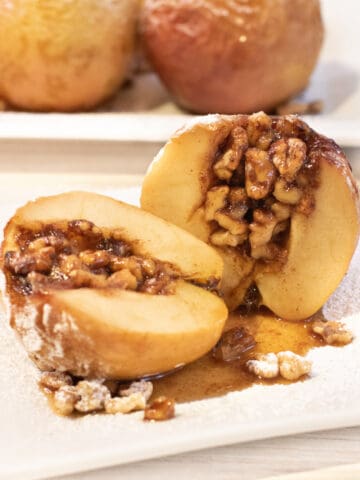 a halved baked apple with walnuts inside on a plate.