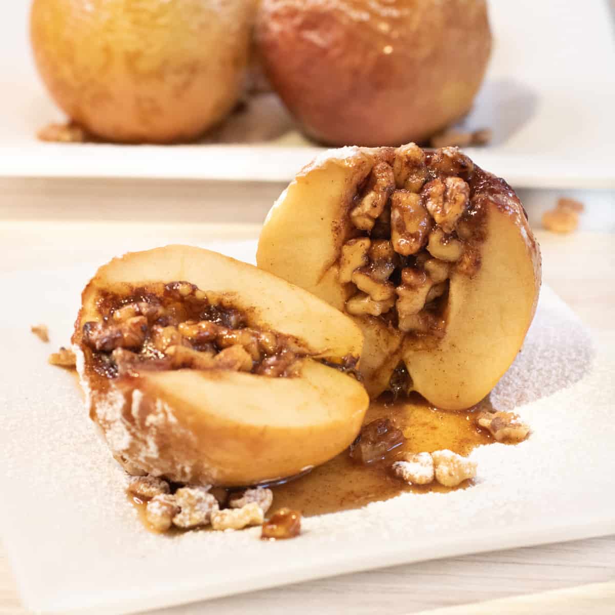 a halved baked apple with walnuts inside on a plate.