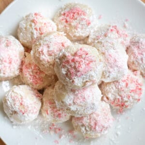 an overhead of a plate of stacked snowball cookies with crushed candy cane on top.