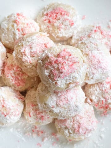 an overhead of a plate of stacked snowball cookies with crushed candy cane on top.